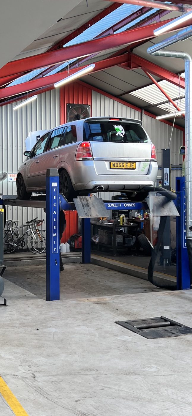 A silver Vauxhall Zafira raised on a blue two-post lift inside the Drive-In workshop