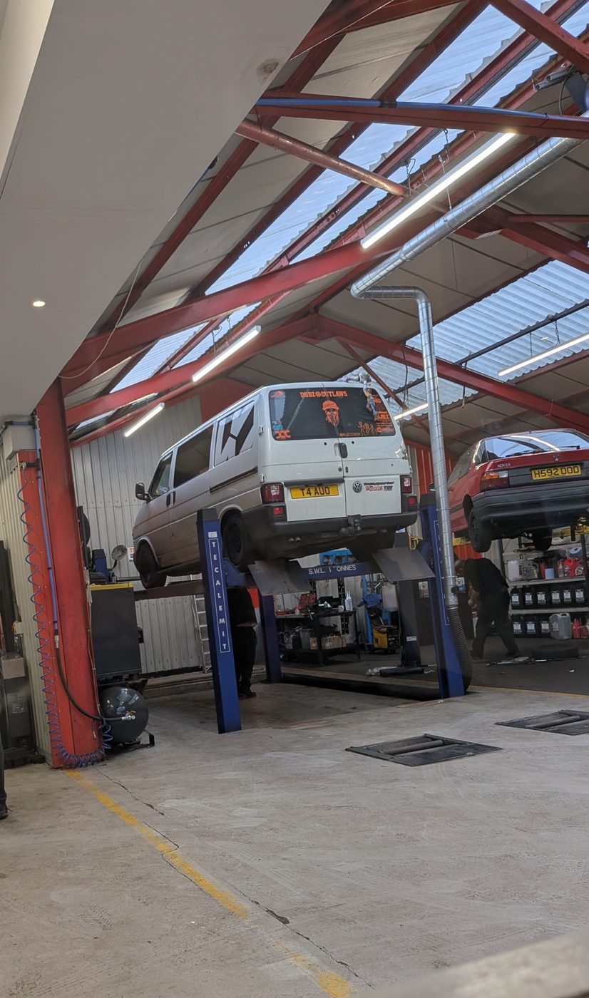 A white VW Transporter van lifted on a ramp in the Drive-In workshop